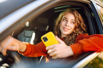 Young woman is driving a car with phone. Leisure, travel, technology, navigation.