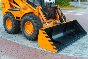 A new yellow mini loader with a bucket on the street during the exhibition of new models of equipment. The mini-escalator works in the city.