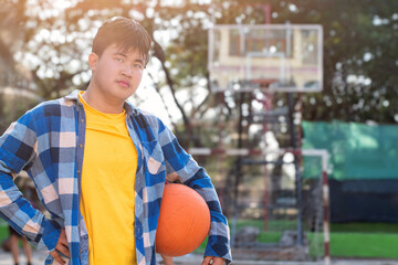 Asian boys in plaid shirt holding and playing basket ball with friends at outdoor basketball court...