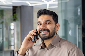 A cheerful professional man is engaged in a friendly phone conversation, smiling in a modern office...