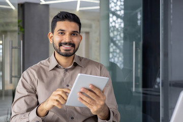 Confident young professional man holding a tablet, smiling and looking approachable in a bright,...