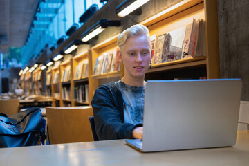 Portrait of a handsome young programmer working remotely on a netbook in a library interior,...