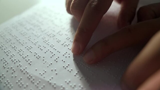 Hand of a blind person reading some braille text on page paper to learn. Finger of blind student touching the braille alphabet Code on sheet. Disabled person concept.