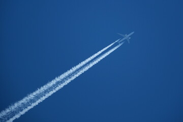 Airplane in the blue sky with contrails in the air. - obrazy, fototapety, plakaty
