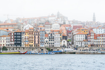 Fototapeta na wymiar Porto, Portugal Skyline, the old town of Porto from across the Douro River. Colorful houses of Porto Ribeira, traditional facades, old multicolored houses with red tiles during a foggy day, Portugal.