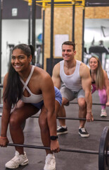 Group of multiracial smiling people doing dead lift with some bars with discs inside a gym, front view, sport dress, vertical image. Fitness and healthy lifestyle concept