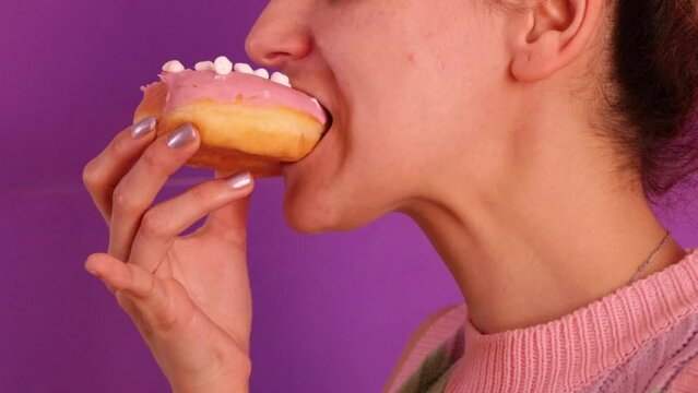 Slow motion video of young woman biting a doughnut and chewing it on pink background