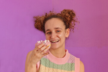 Pretty young caucasian woman smiling holding a donuts looking at camera and a candy colored T-shirt on pink background