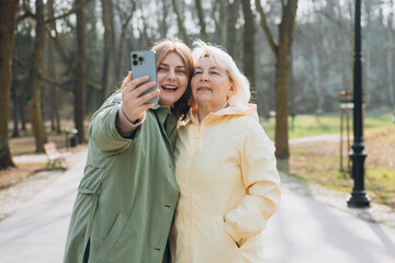 Happy older Mother and adult positive daughter are doing Selfie on city street, Urban lifestyle concept. Travelers. Outdoor shot of well-dressed female friends. Family day