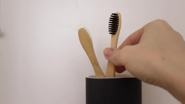 Bathroom organization, hand putting eco toothbrush in a glass, wooden cabinet, sustainable oral care