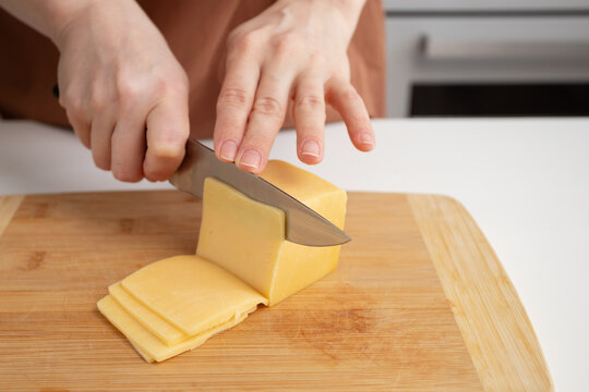 Woman preparing lunch, slicing cheese with a knife on a cutting board in the kitchen - Powered by Adobe