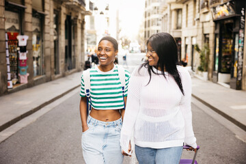 A young female couple is exploring a new city during a short weekend trip, walking together while...