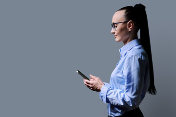 Profile view 30s woman using smartphone on grey background