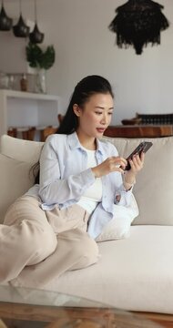 Pretty Asian woman holding smart phone editing photos using apps, chatting on-line with friends, making purchases via popular marketplaces enjoy modern wireless gadget usage for communication or fun
