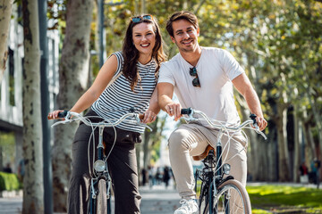 Happy loving couple cycling while looking at camera in the city