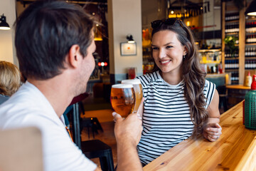 Pretty young couple toasting with beer while looking each other at the bar - 790066821
