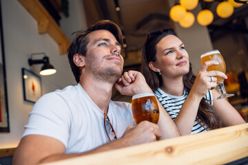 Pretty young couple toasting with bottle beer while looking forwards the bar - 790066823