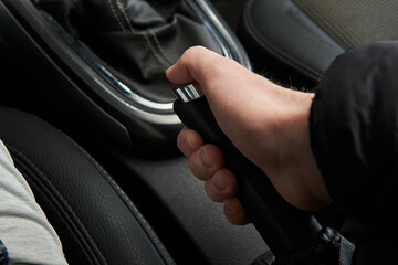 Man holding and pulling handbrake handle emergency parking e-brake in the black car interior