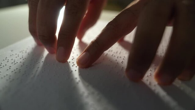 Close up hand of a blind person reading some braille text on page paper to learn. Finger of blind student touching the braille alphabet Code on sheet. Disabled person concept.