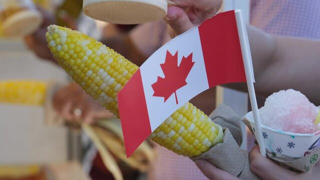 Canada Surrey Hot corn and Canada flag sprinkle salt on the corn Canada Day Families, people dressed in red, walk in the square on a holiday weekend