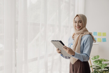 Asian Muslim businesswoman uses calculator and writes notes with mathematical financial...