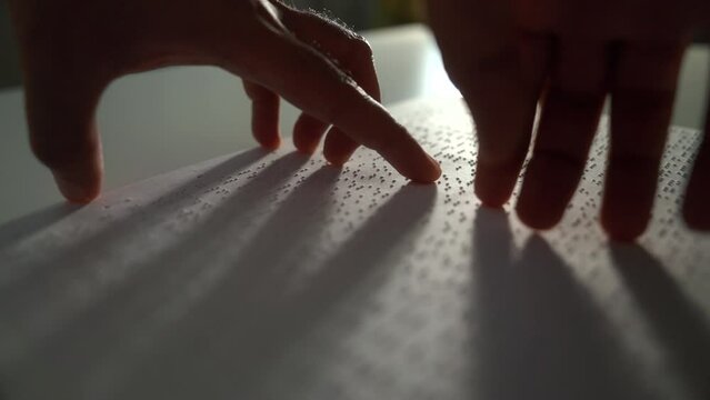 Close up hand of a blind person reading some braille text on page paper to learn. Finger of blind student touching the braille alphabet Code on sheet. Disabled person concept.