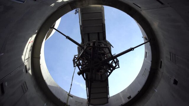Low angle shot of a CRANE stacking concete components on a WIND TURBINE TOWER construction filmed from the inside of the tower while it being built round building inside a grain silo gas reservoir 4K
