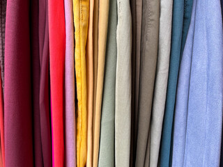 A close-up of a row of colorful trousers. Side view of pants on a hanger in a store.