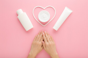 Young adult woman hands, white cream jar, bottle, tube and heart shape on pink table background. Pastel color. Care about clean and soft female body skin. Closeup. Point of view shot. Top down view. - 790103228