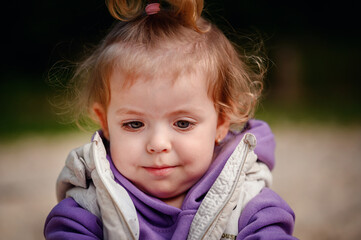 Close-up of a toddler with a subtle smile, her eyes filled with curiosity, framed by a tousled...