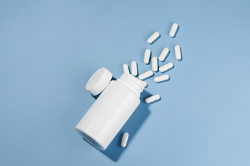 White mockup jar and spilled pills on blue isolated background. The concept of treatment from...
