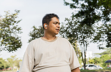hombre latino mirando a un costado mientras esta en el parque y usa sus audifonos 