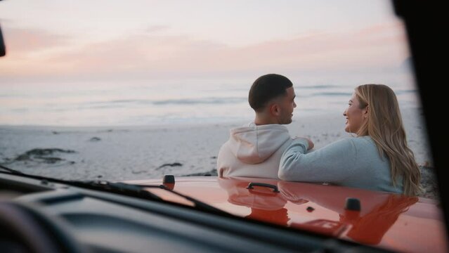 Rear view of young loving couple on vacation standing by car at beach watching morning sunrise on road trip  - shot in slow motion