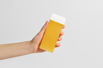 A woman's hand holds a yellow cassette for depilation on a white background. The concept of beauty, body hair removal, aesthetic procedures, materials.
