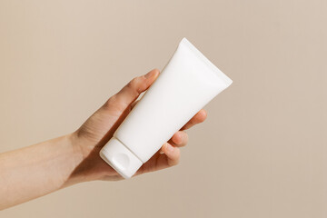 Female hand holding white tube mockup on beige isolated background. Concept of beauty, aesthetics, skin care products.