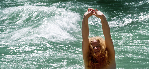 redhead adult mature woman with raised outstretched arms enjoying the summer vacation feeling by the raging waters of the verdon river in france