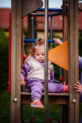 Obraz premium A focused toddler with a determined expression navigates playground equipment, her lilac outfit adding a pop of color to the outdoor play area