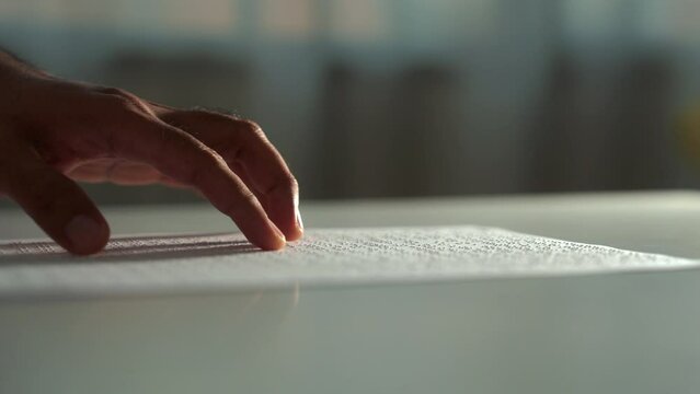 Close up hand of a blind person reading some braille text on page paper to learn. Finger of blind student touching the braille alphabet Code on sheet. Disabled person concept.