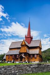 Fototapeta na wymiar View of the 13th century medieval Ringebu Stave Church stands amidst headstones under a blue sky with clouds in Summer, echoing centuries of Norwegian heritage.