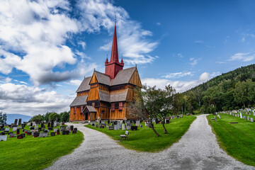 View of the 13th century historic Ringebu Stave Church stands amidst headstones under a blue sky...