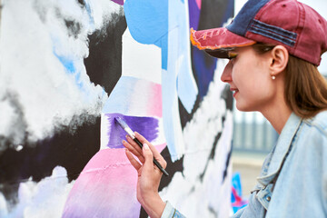 Female painter draws picture with paintbrush on canvas for outdoor street exhibition, close up side view of female artist apply brushstrokes to canvas, symphony of art creativity