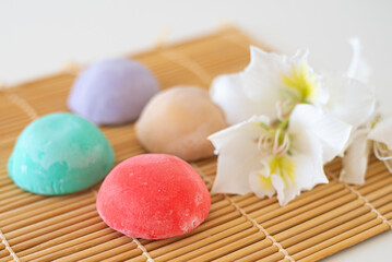 Four mochi different tastes and colors on bamboo makisu with flowers on light background. Japanese traditional frozen delicious dessert mochi. ice cream with dough of sticky rice. asian cuisine