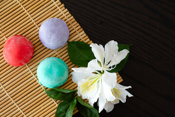Three mochi different tastes and colors on bamboo makisu with flowers on black background. Japanese traditional frozen delicious dessert mochi. ice cream with dough of sticky rice. Asian cuisine.
