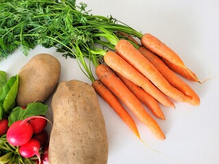 Bunch of carrots, potatoes and radish on a creamy background.