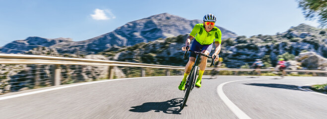 Mature Adult on a racing bike climbing the hill at mediterranean sea landscape coastal mountain road - mallorca mountains. high speed motion blur effect
