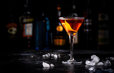 Orange alcoholic hard cocktail drink with scotch whiskey, vermouth and liquor in martini glass, dark bar counter background - 790155697