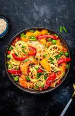 Stir fry noodles with shrimps, colorful paprika, green pea, chives and sesame seeds with ginger, garlic and soy sauce. Black table background, top view