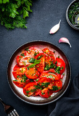 Simple summer juicy tomato salad with parsley, dill, garlic and olive oil dressing, black stone table background, top view - 790155839