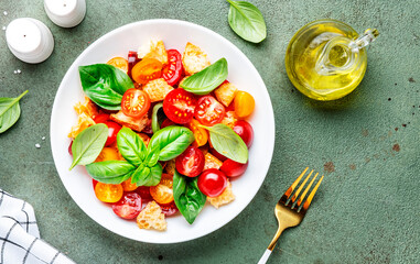 Simple summer salad with with stale bread, cherry tomatoes, olive oil, sea salt and green basil, stone table background, top view