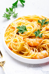 Delicious spaghetti pasta with big shrimp on plate with parsley, white table background. Top view